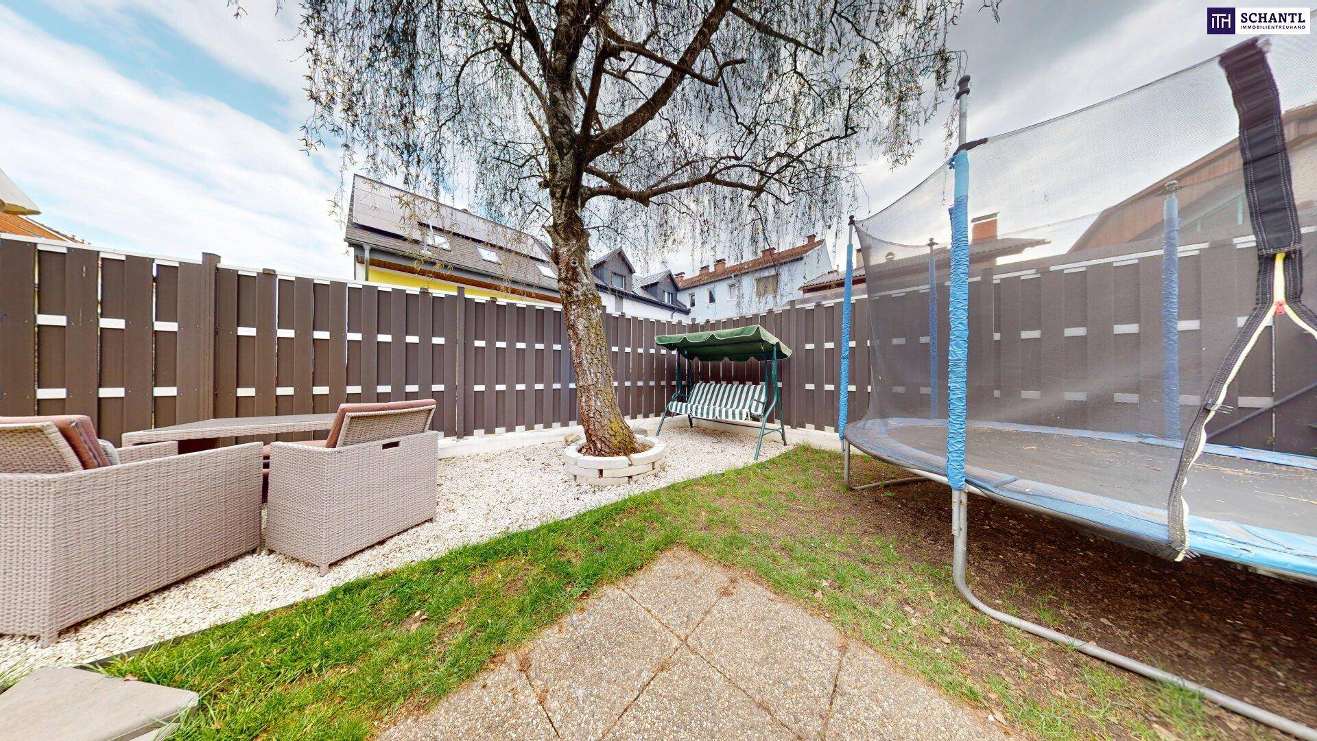 Gepflegter Gartenbereich mit Sitzgelegenheiten, Schaukel und Trampolin, umgeben von einem Holzzaun.