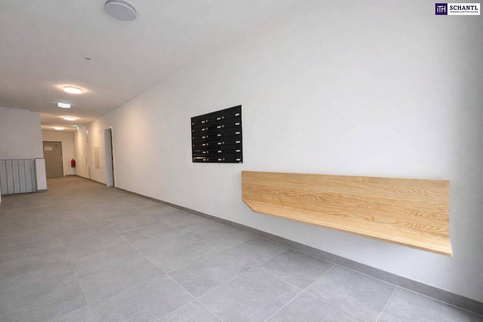 Heller Flur im Gebäude mit Briefkästen und einer schlichten Holzbank.
