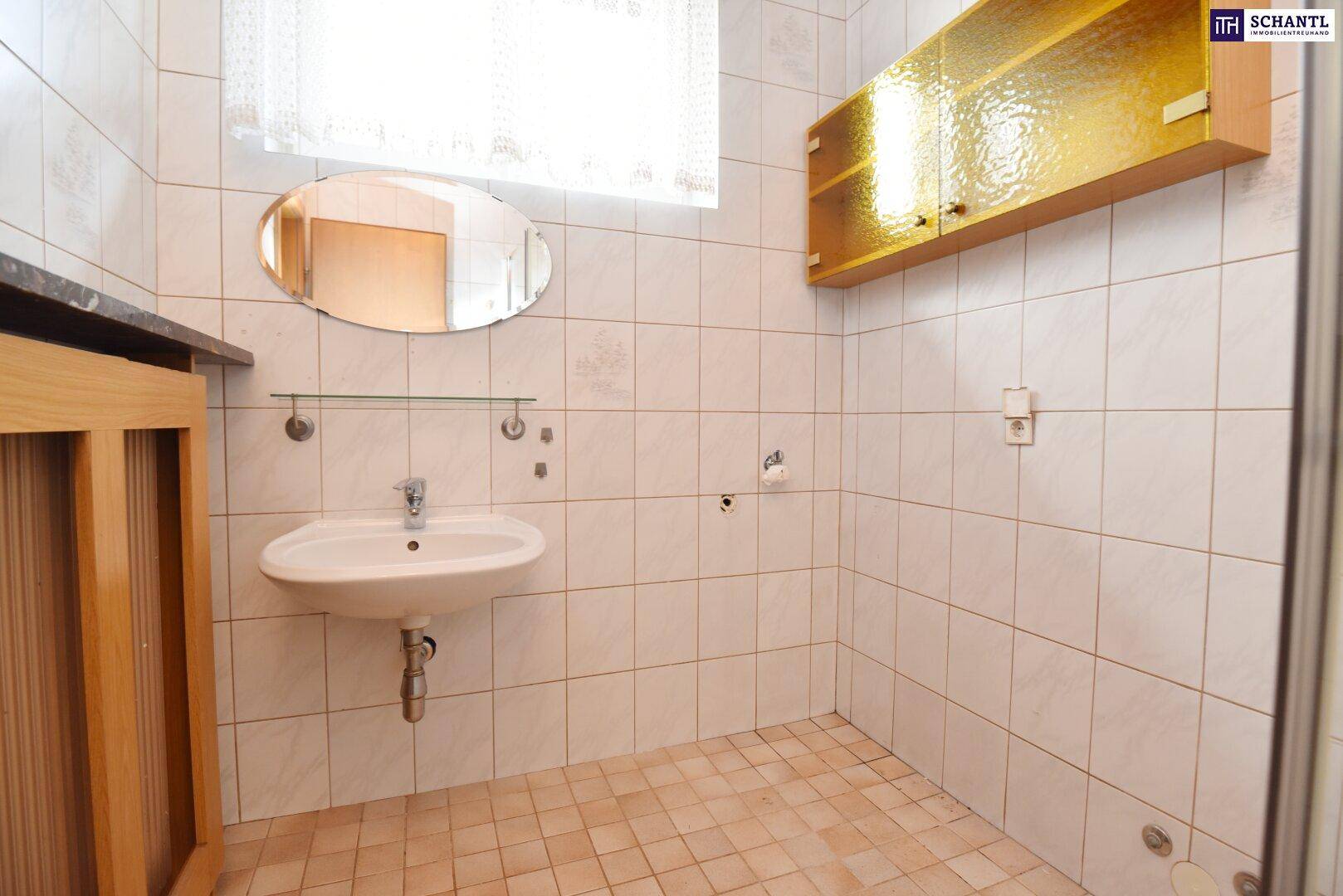 Badezimmer mit Waschbecken, Spiegel und Fenster, gefliest in hellen Tönen.