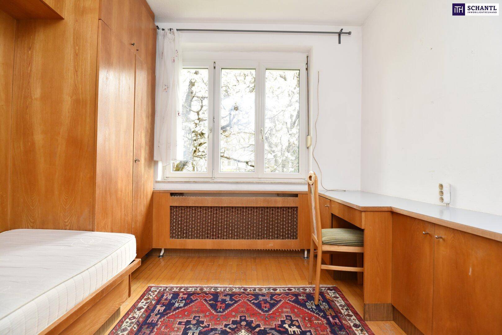 Kinderzimmer oder Büro mit Holzbett, Schreibtisch und Fensterblick ins Grüne.