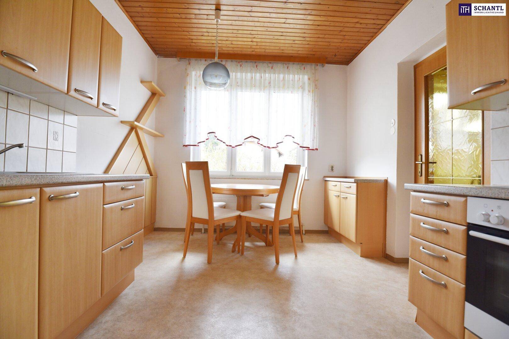 Helle Küche mit Holzschränken, Essbereich und Fensterblick ins Grüne.
