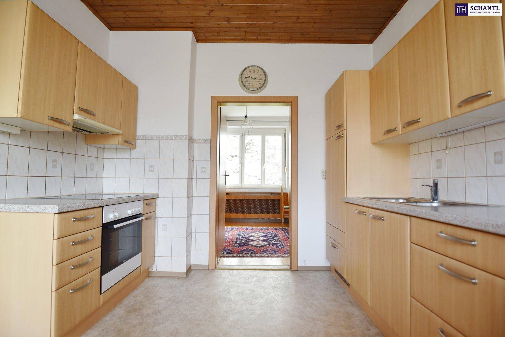 Küche mit Holzschränken, Fliesenrückwand und Durchgang zu einem weiteren Zimmer.