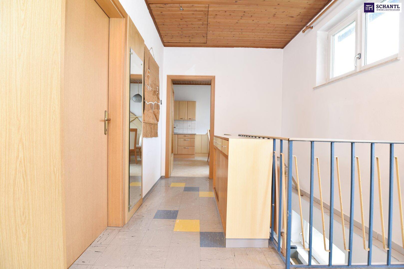 Flur mit Holzdecke, bunten Bodenfliesen und Treppenaufgang.