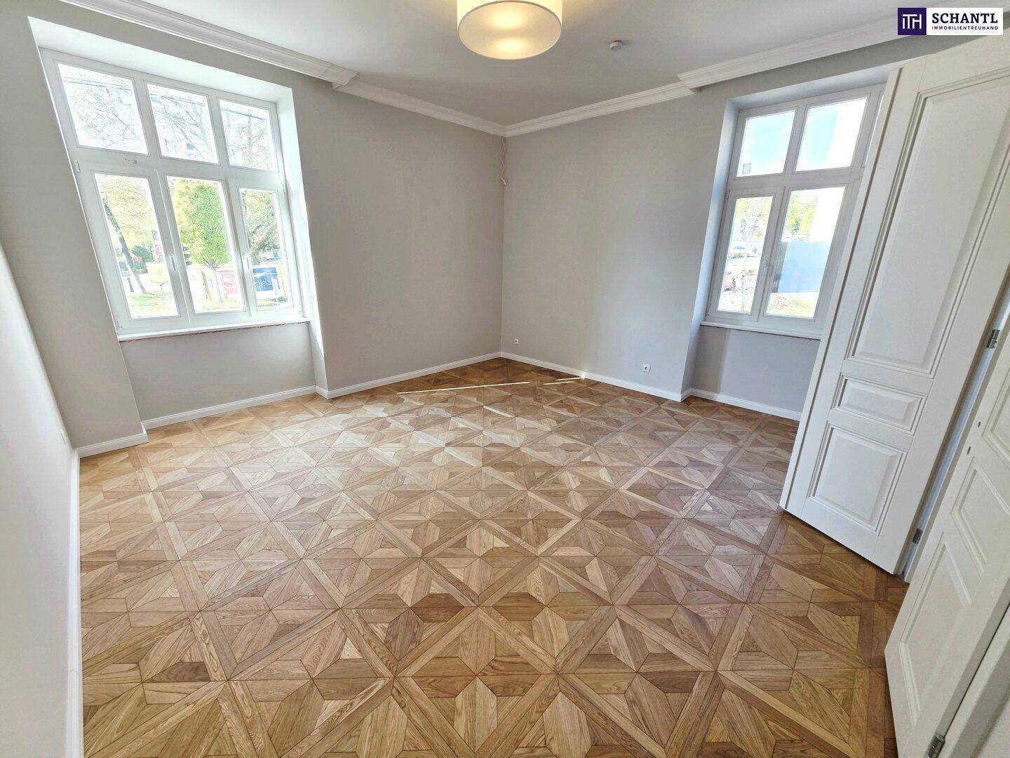 Helles Zimmer mit elegantem Parkettboden und hohen Fenstern, das viel Tageslicht hereinlässt.