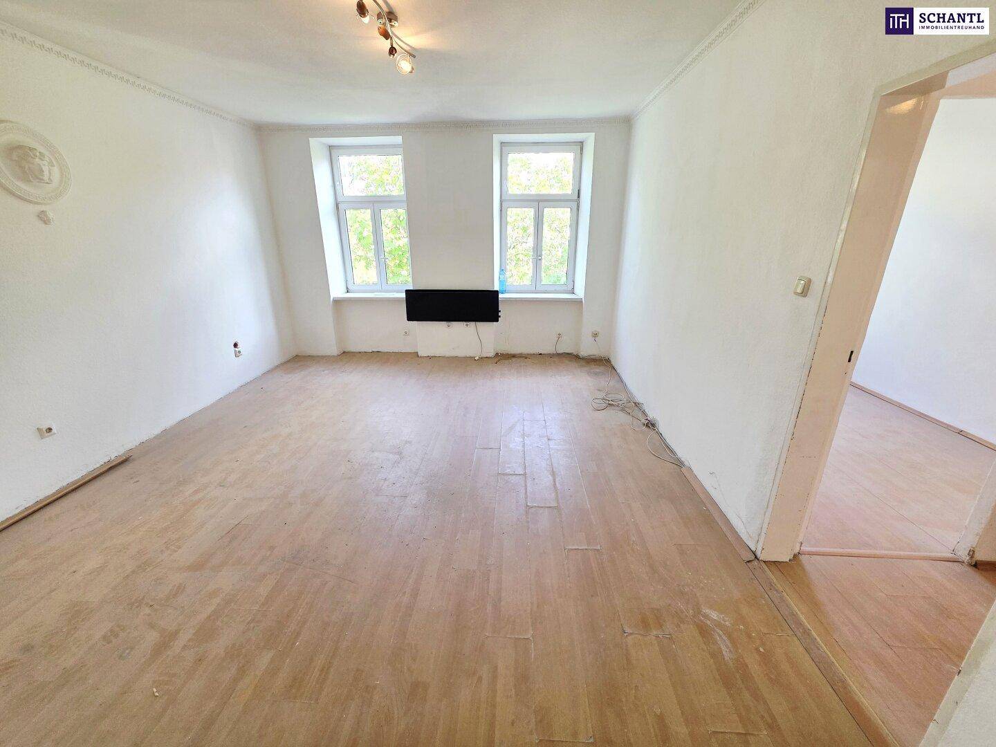 Heller Wohnraum mit Holzboden und zwei Fenstern, die viel Tageslicht hereinlassen.
