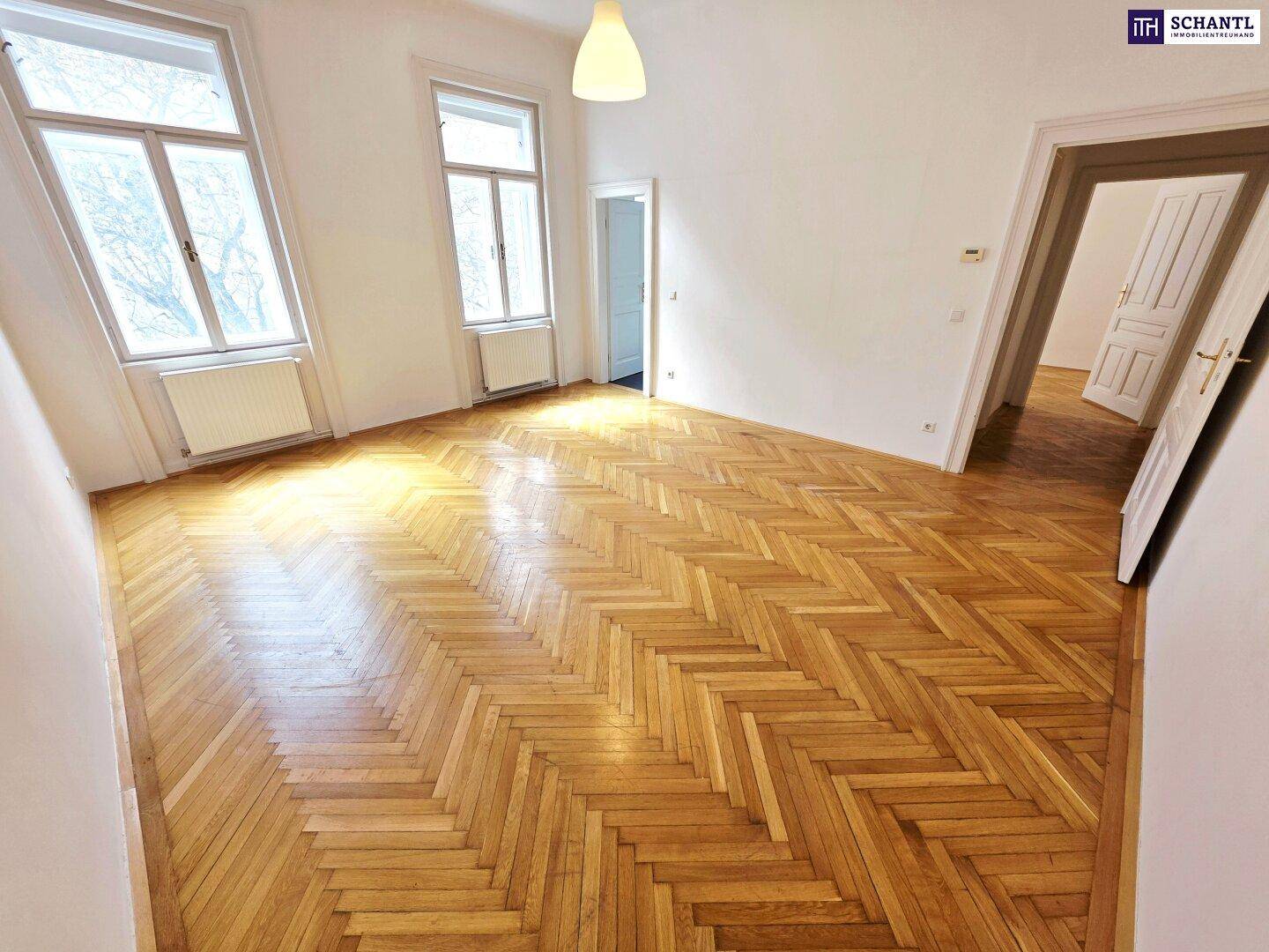 Geräumiges Zimmer mit klassischem Fischgrätparkett und hohen Fenstern, die viel Licht hereinlassen.