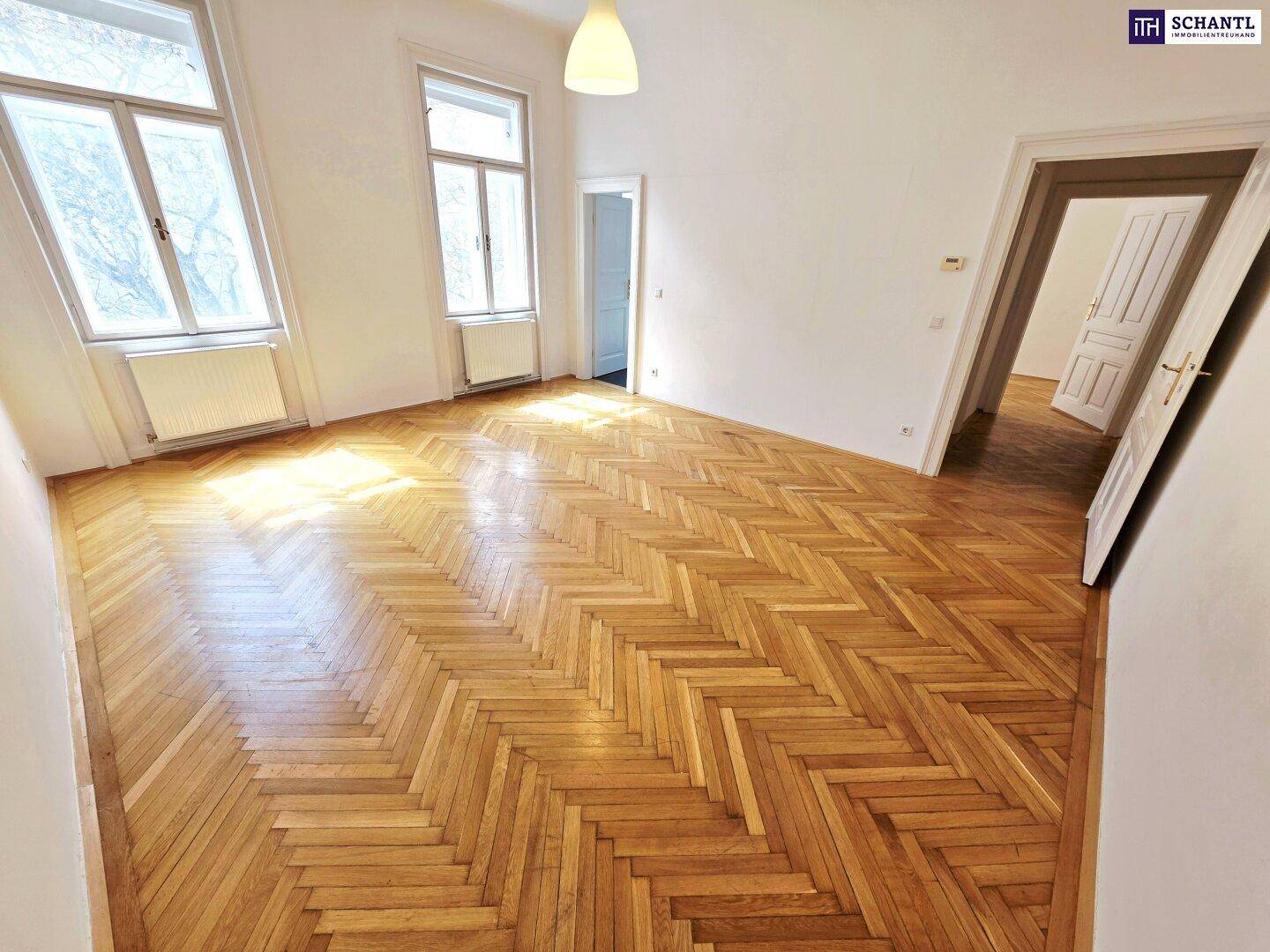 Heller Raum mit glänzendem Fischgrätparkett und hohen Fenstern, die den Raum erhellen.