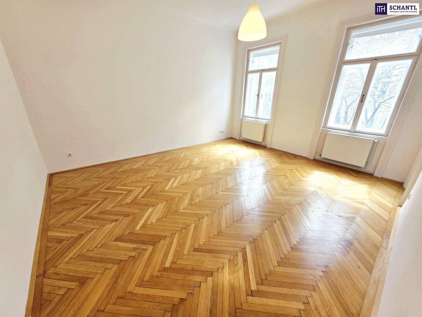 Helles Zimmer mit klassischem Fischgrätparkett und hohen Fenstern, die den Raum mit Licht füllen.