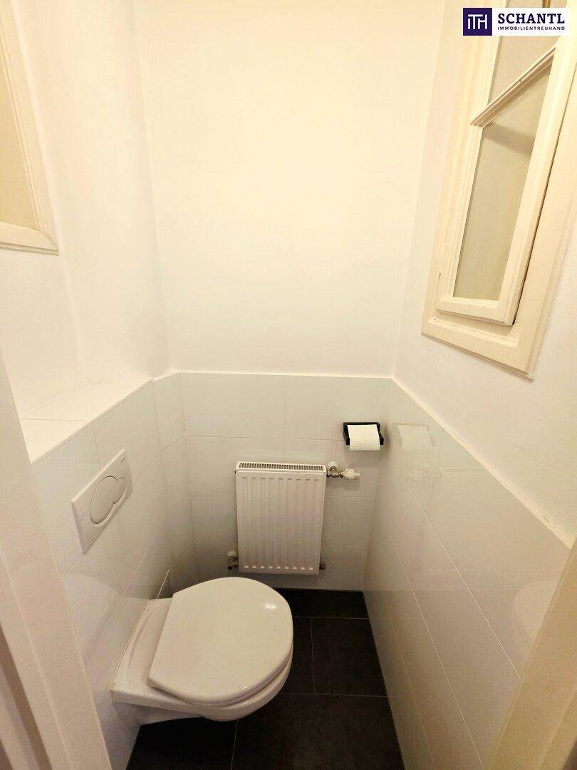 Kleines Gäste-WC mit wandhängender Toilette, Fenster und dunklem Fliesenboden.