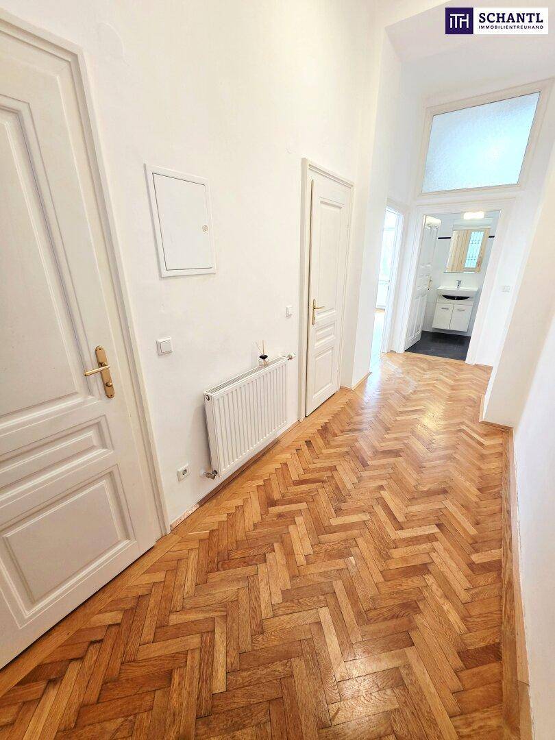 Langer Flur mit Fischgrätparkett und Zugang zu verschiedenen Räumen, inklusive Badezimmer.