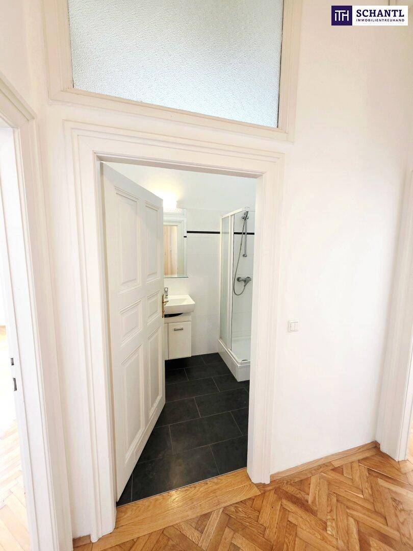 Blick vom Flur in ein modernes Badezimmer mit Duschkabine und Waschbecken.