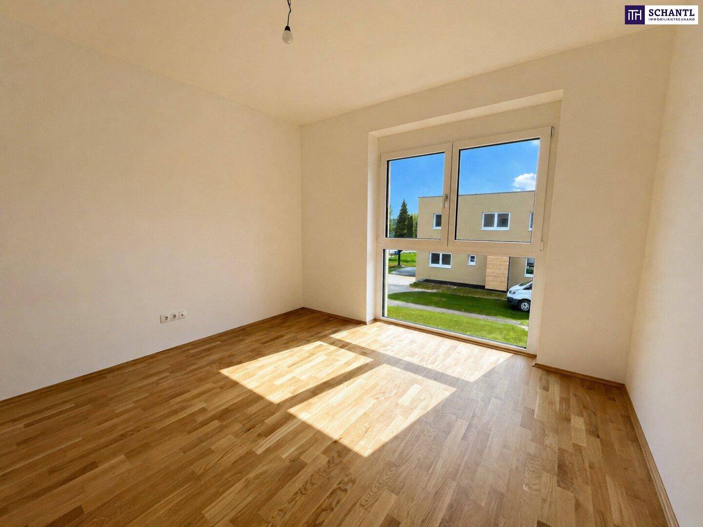 Helles Schlafzimmer mit Parkettboden und großem Fenster, das einen Blick auf die Nachbarschaft bietet.