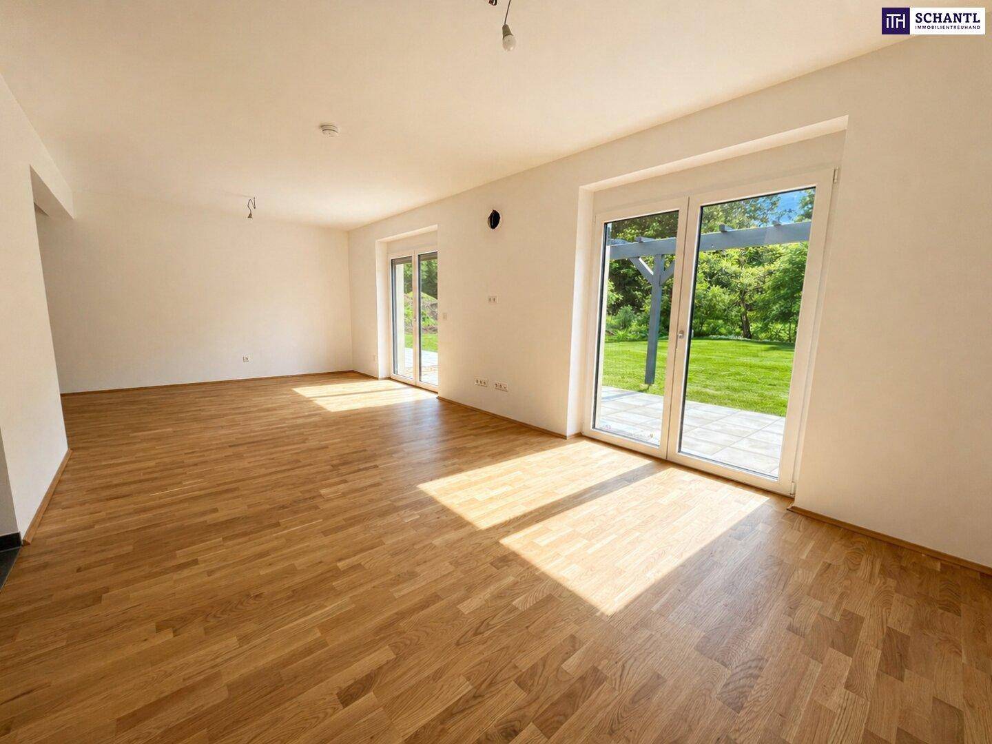 Geräumiges Wohnzimmer mit hellem Parkettboden und zwei Zugängen zur Terrasse oder zum Gartenbereich.