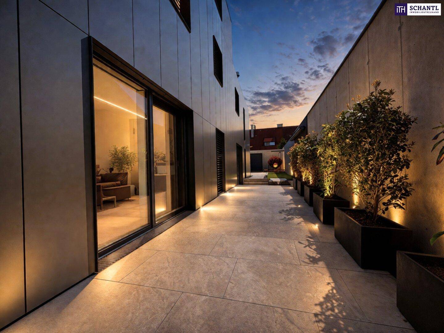 Beleuchteter Weg entlang der modernen Hausfassade mit Pflanzenkübeln.