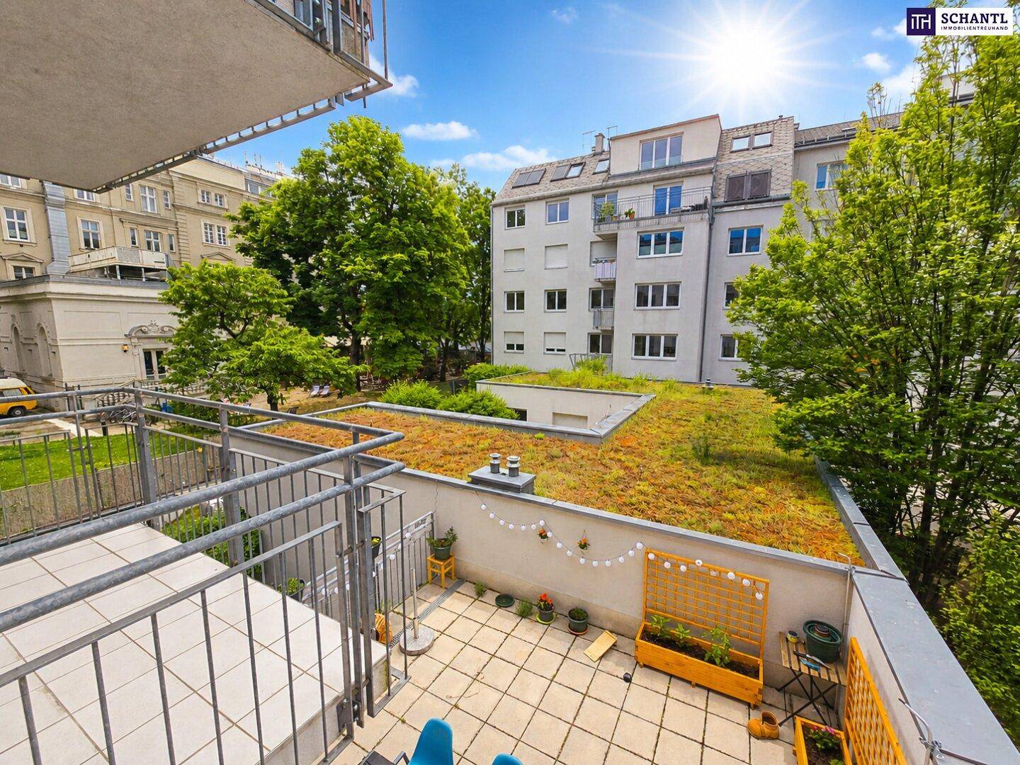 Geräumiger Balkon mit Fliesenboden, Pflanzen und weitem Blick auf grüne Dächer und die Umgebung.