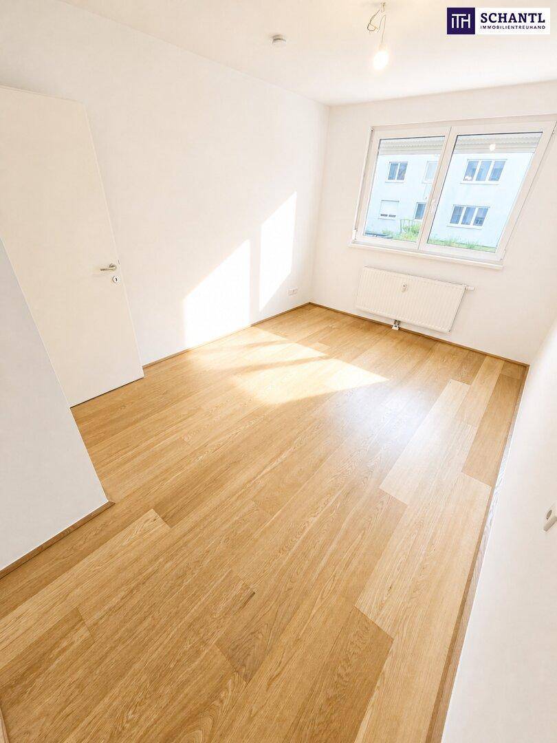 Lichtdurchflutetes Zimmer mit hellem Parkettboden und großem Fenster, ideal als Schlafzimmer oder Büro.