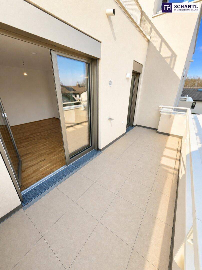 Balkon mit Zugang zu einem hellen Innenraum mit Holzfußboden durch eine große Schiebetür.