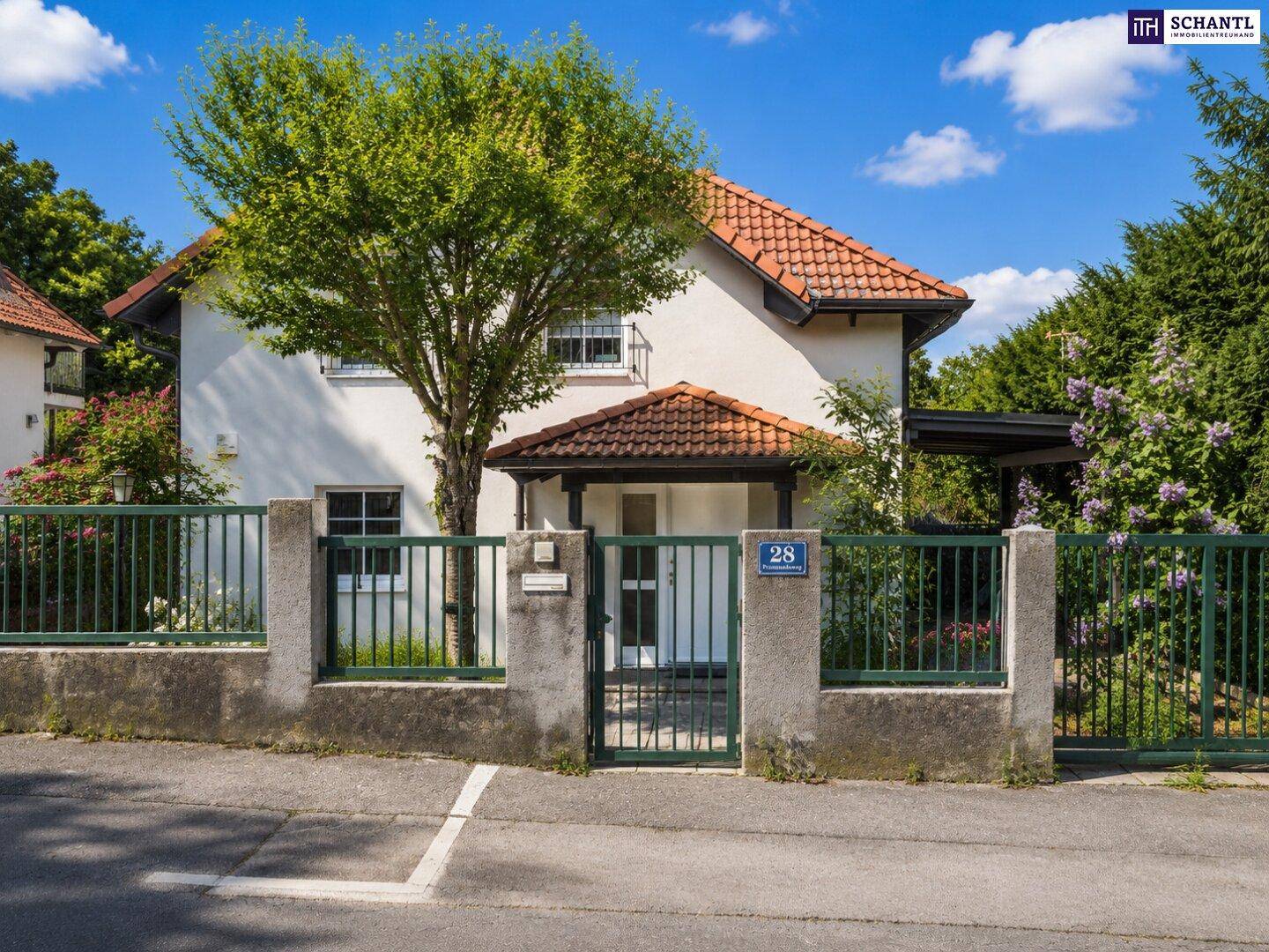 Einfamilienhaus von der Straße aus gesehen, mit Vorgarten, Zaun und Carport unter einem Baum.