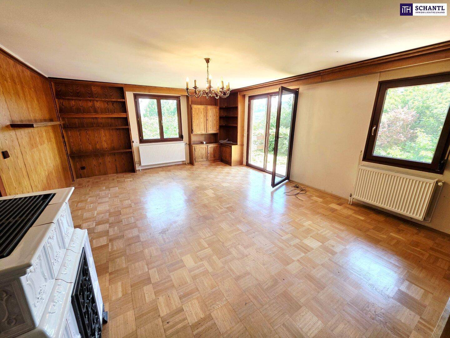 Geräumiges Wohnzimmer mit Parkettboden, Kachelofen und großen Fenstern zum Garten.