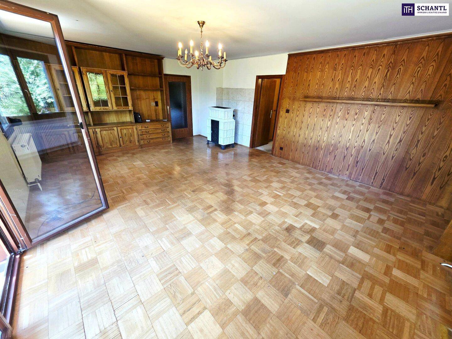 Wohnzimmer mit Parkettboden, Holzeinbauten und traditionellem Kachelofen.