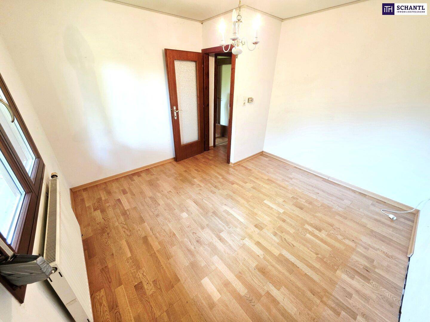 Helles Zimmer mit Parkettboden, weißen Wänden und Fenster mit Blick ins Grüne.