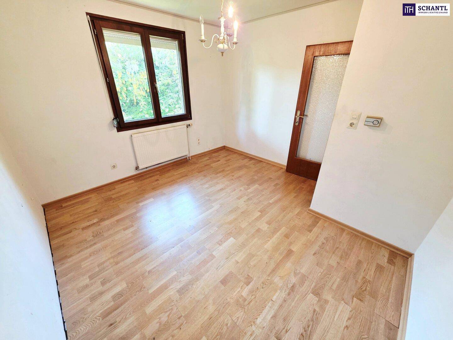 Freundliches Zimmer mit Parkettboden, Fenster und schlichter Einrichtung.