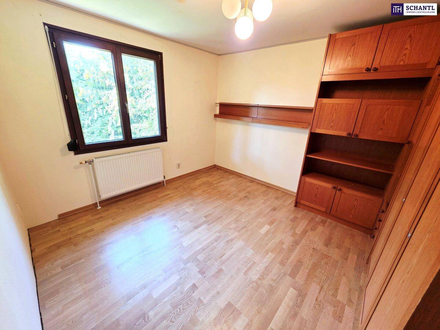 Schlafzimmer mit Parkettboden, Einbauschrank und Fenster mit Blick ins Grüne.