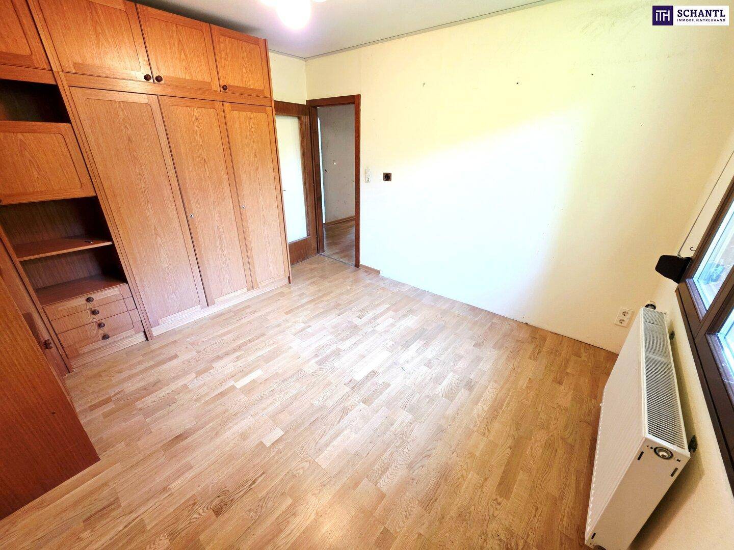 Schlafzimmer mit Parkettboden, großem Einbauschrank und hellem Fenster.