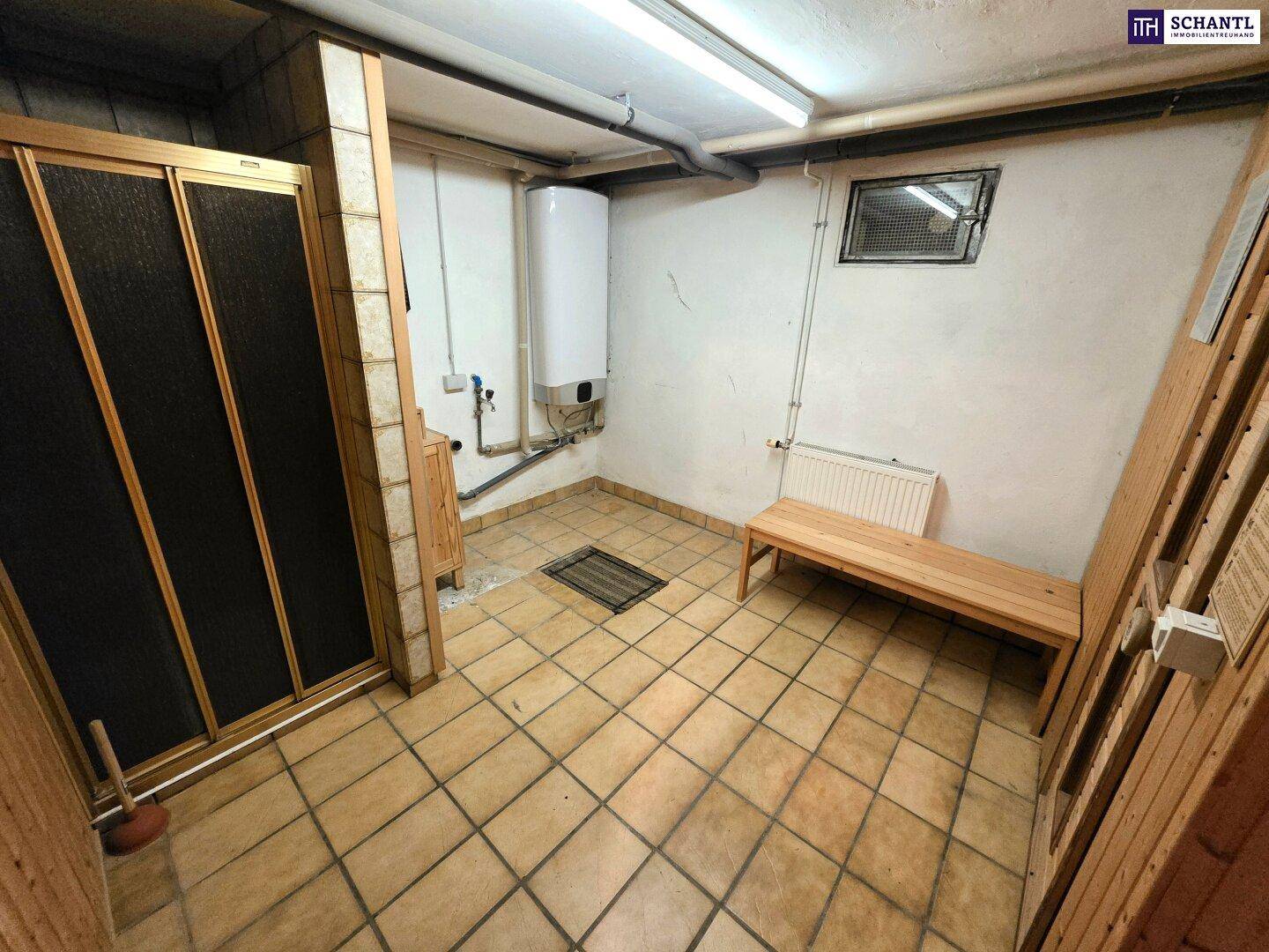Kellerraum mit Fliesenboden, Sitzbank und Warmwasserboiler, möglicherweise als Wellnessbereich nutzbar.