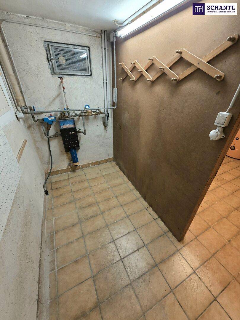 Technischer Kellerbereich mit Fliesenboden, sichtbaren Wasserleitungen und Zählern.