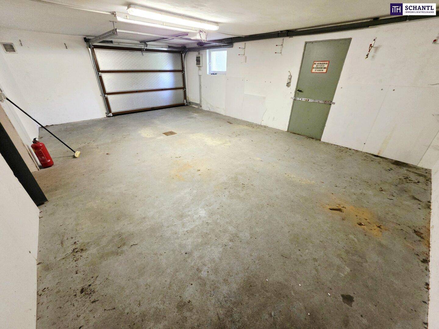 Geräumige Garage mit Betonboden, Rolltor und Feuerlöscher, bietet Platz für Fahrzeuge.