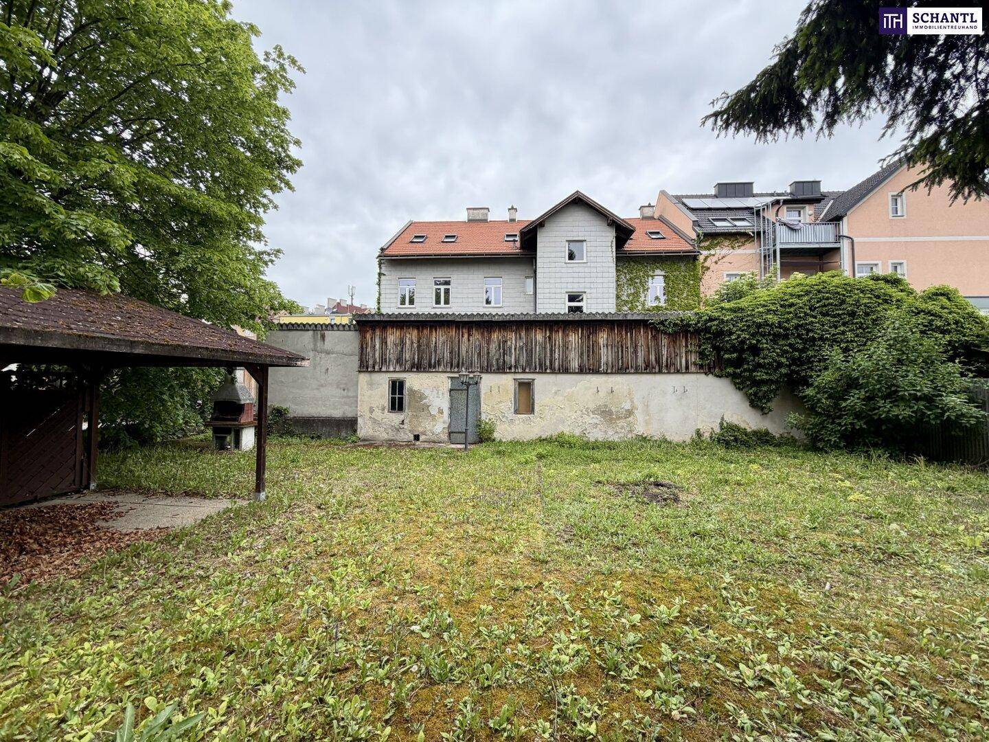 Gartenbereich mit Rasenfläche, einem kleinen Unterstand mit Grill und der Rückseite des Gebäudes.