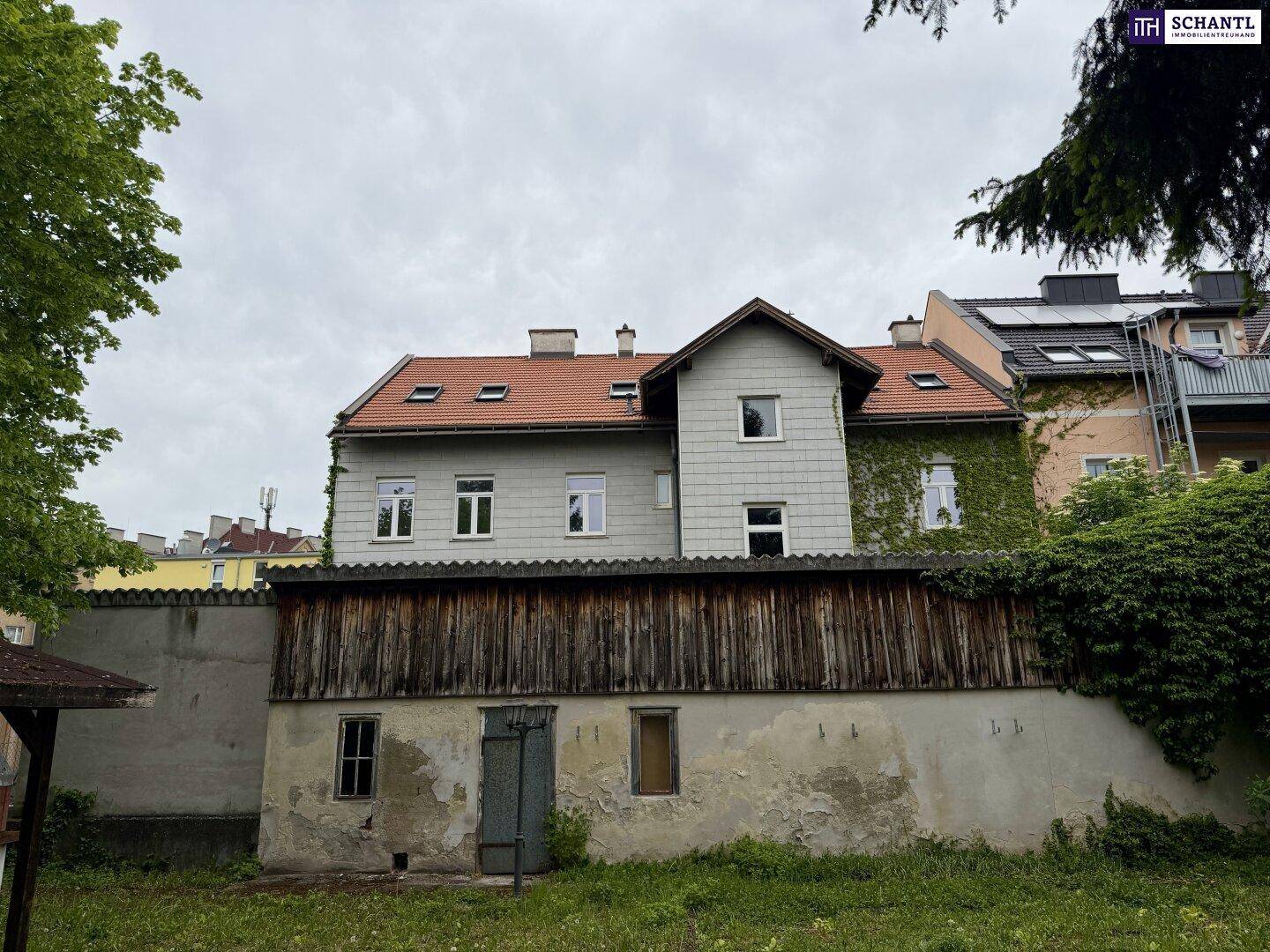 Ruhiger Gartenbereich mit altem Schuppen und der Rückseite des Gebäudes, teilweise mit Efeu bewachsen.