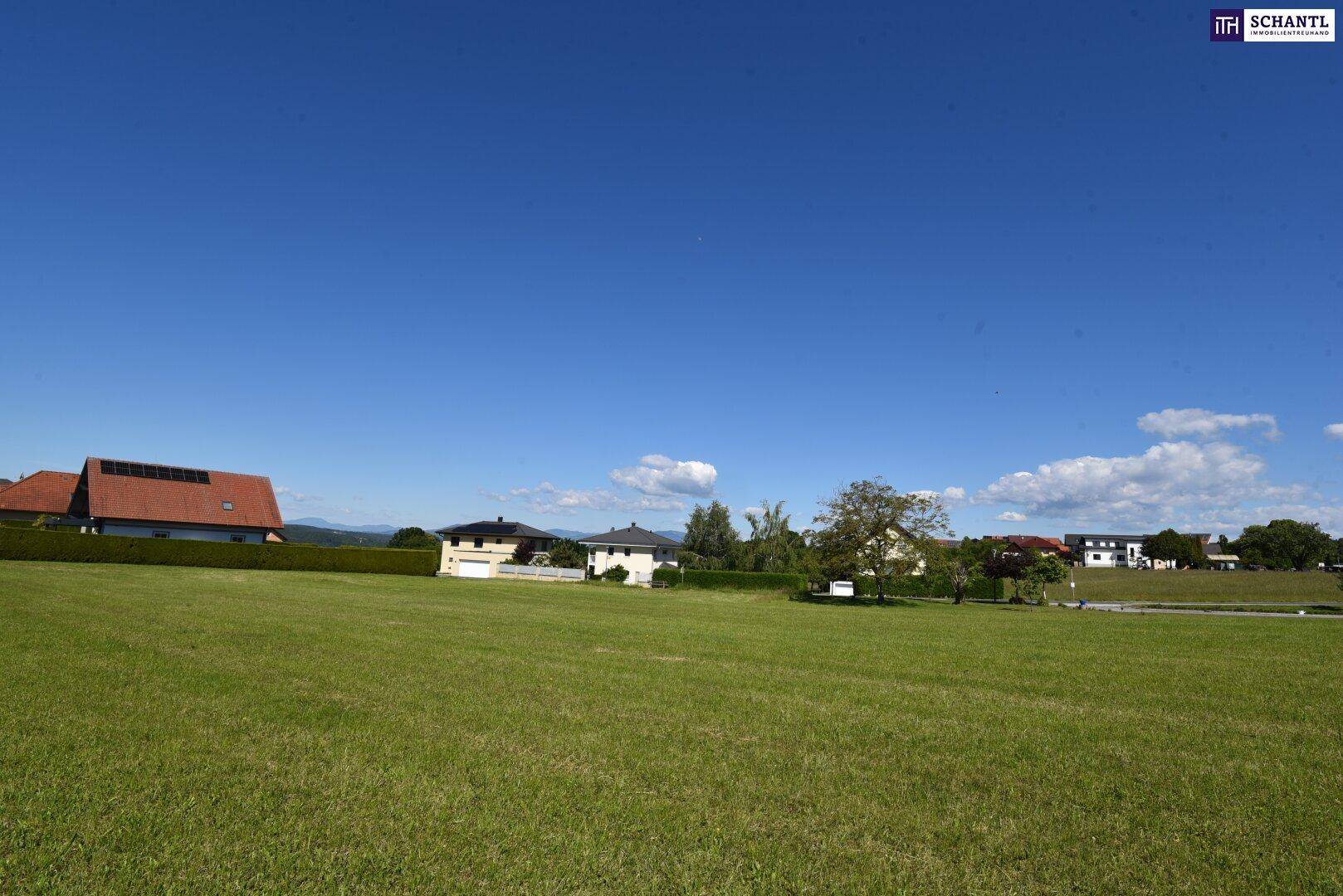 Weitläufige grüne Wiese mit Wohnhäusern und einer malerischen Hügellandschaft am Horizont.
