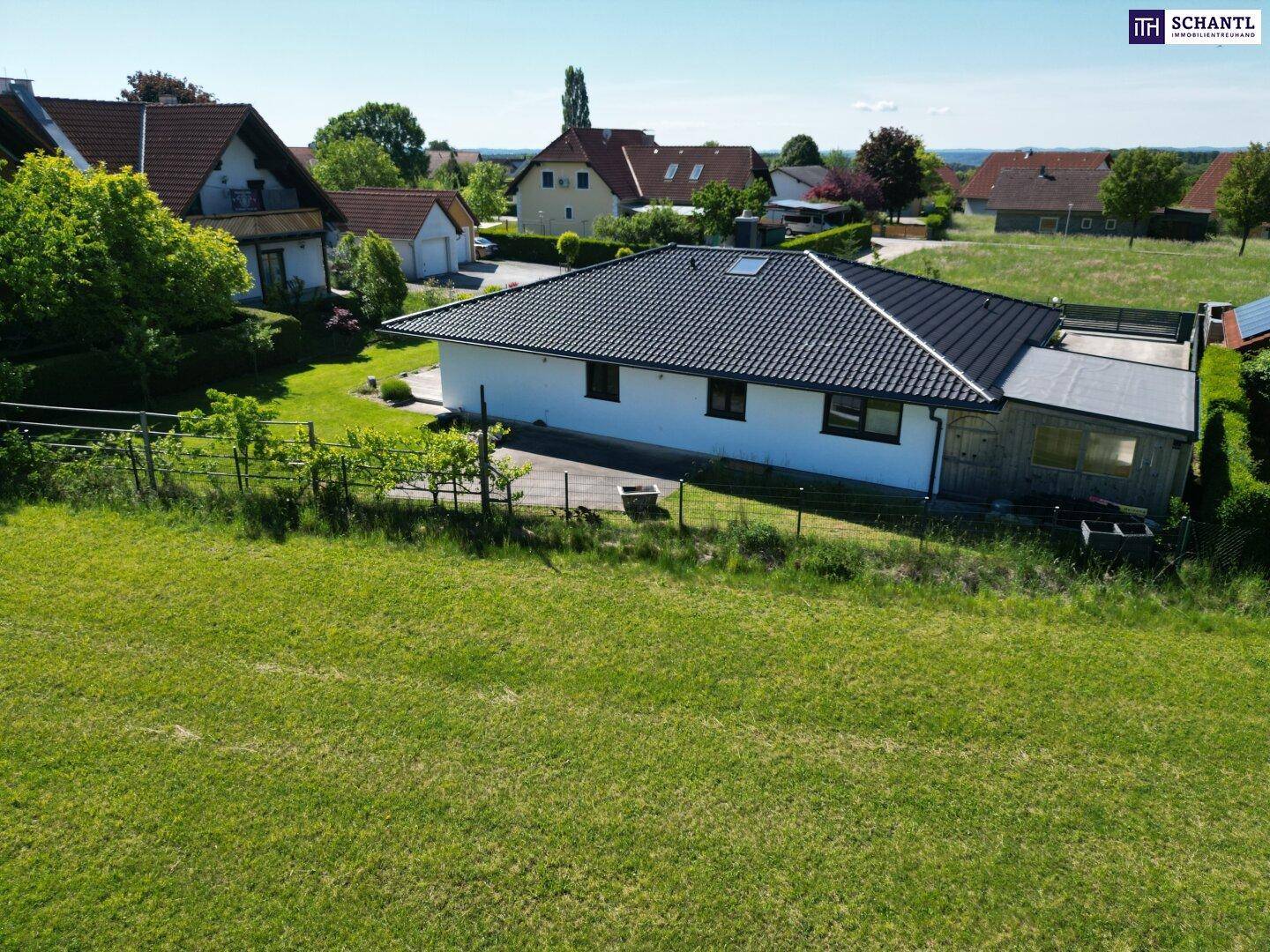 Luftaufnahme eines modernen Einfamilienhauses mit dunklem Dach, umgeben von Grünflächen und Nachbarhäusern.
