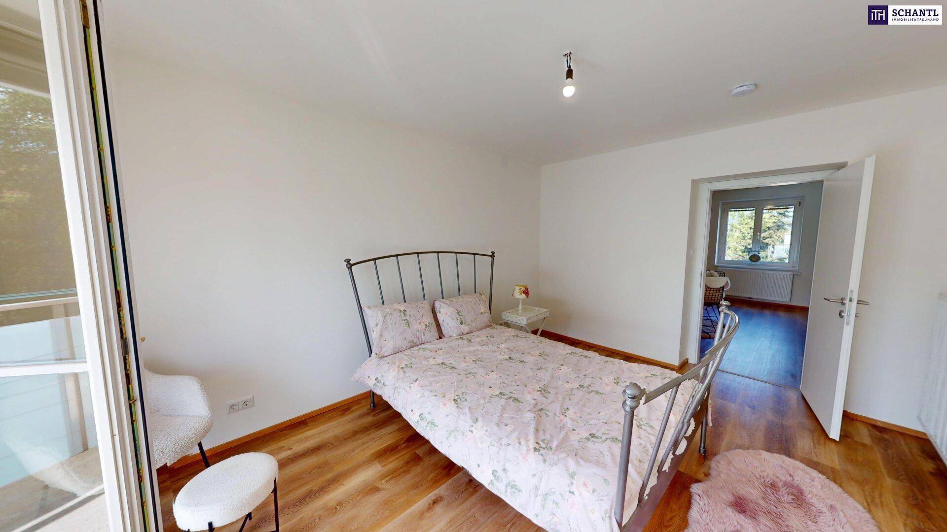 Helles Schlafzimmer mit Holzboden, Doppelbett und Zugang zu einem weiteren Raum.