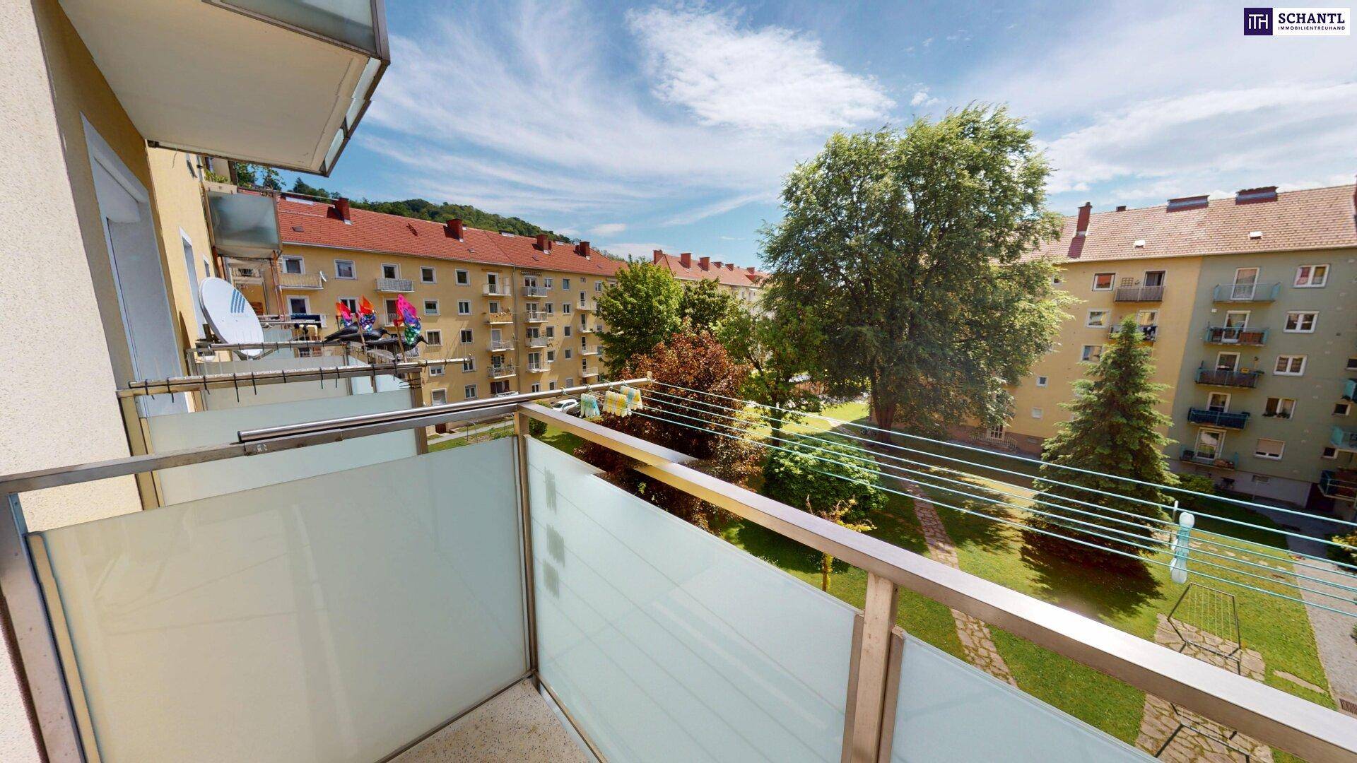 Balkon mit Blick auf einen grünen Innenhof und umliegende Wohngebäude.