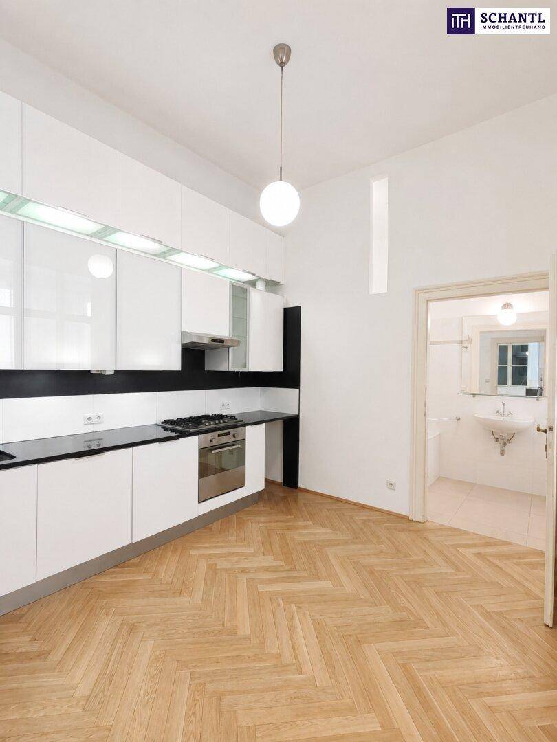 Moderne Küche mit weißen Hochglanzschränken, schwarzer Arbeitsplatte und Gasherd, angrenzend an ein Badezimmer.