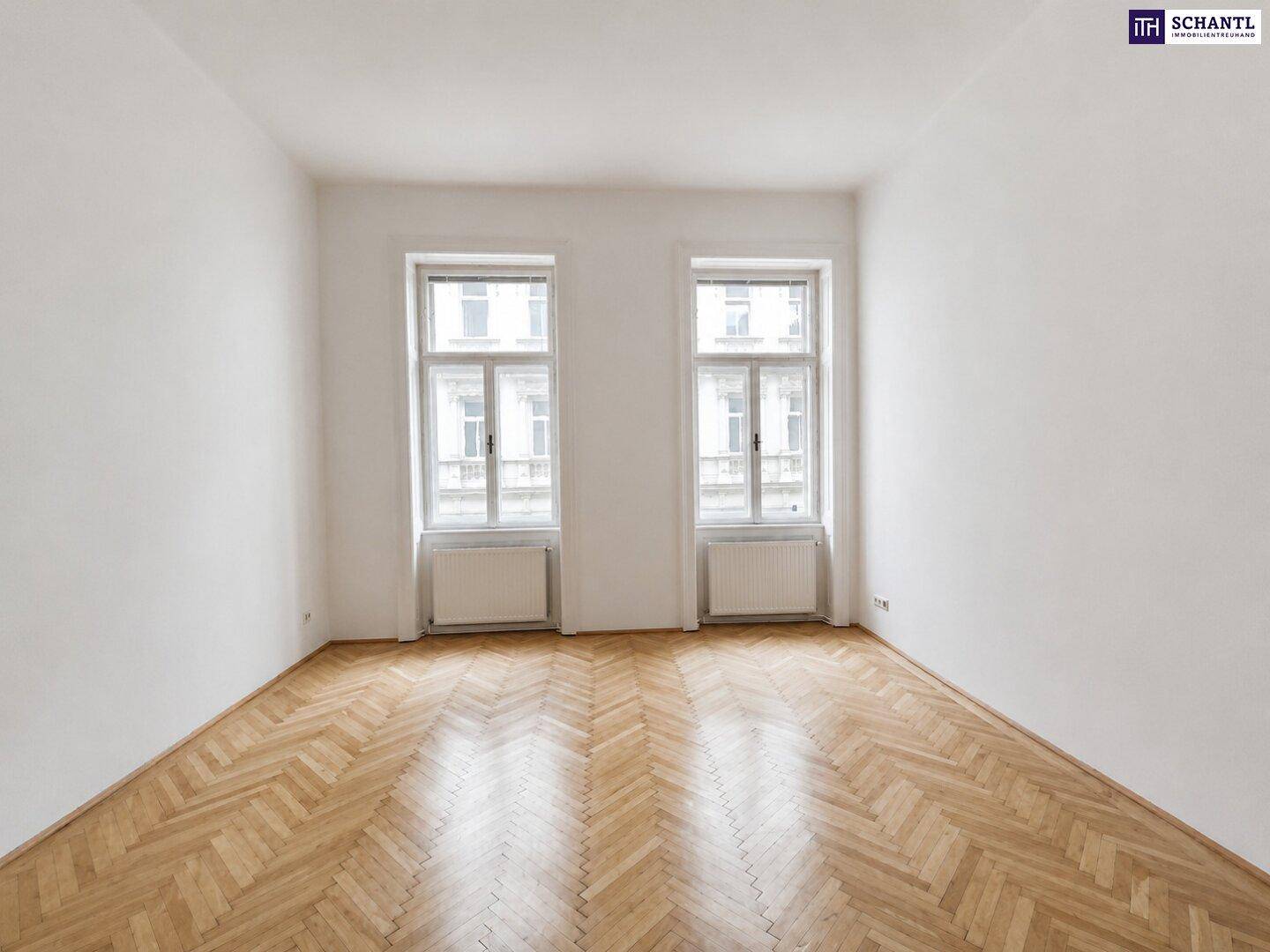 Lichtdurchflutetes Zimmer mit elegantem Fischgrätparkett und zwei Fenstern, ideal für individuelle Gestaltung.