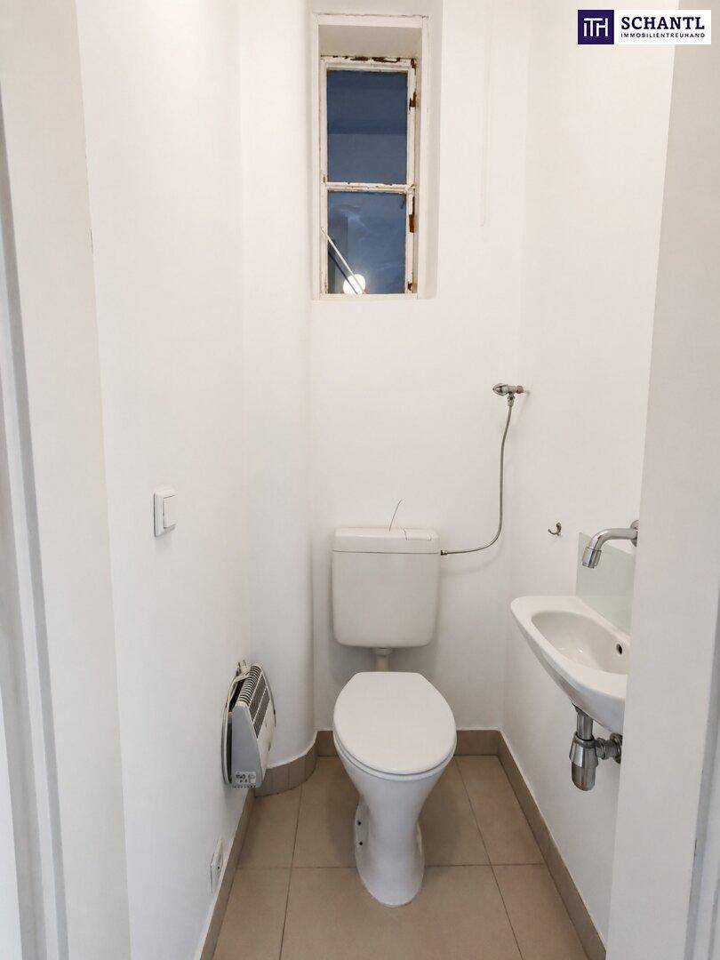 Kleines Gäste-WC mit Toilette, Handwaschbecken und einem hohen Fenster für Tageslicht.