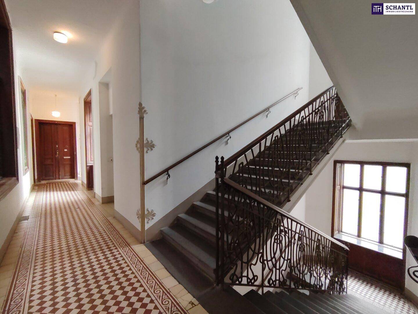 Elegantes Treppenhaus mit kunstvollem schmiedeeisernem Geländer und gemustertem Fliesenboden.