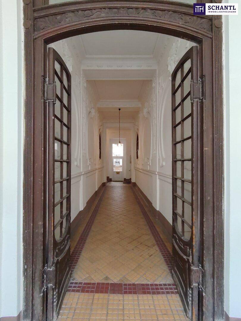 Eingang zu einem prunkvollen Flur durch große Holztüren mit Glaseinsätzen und Stuckverzierungen.