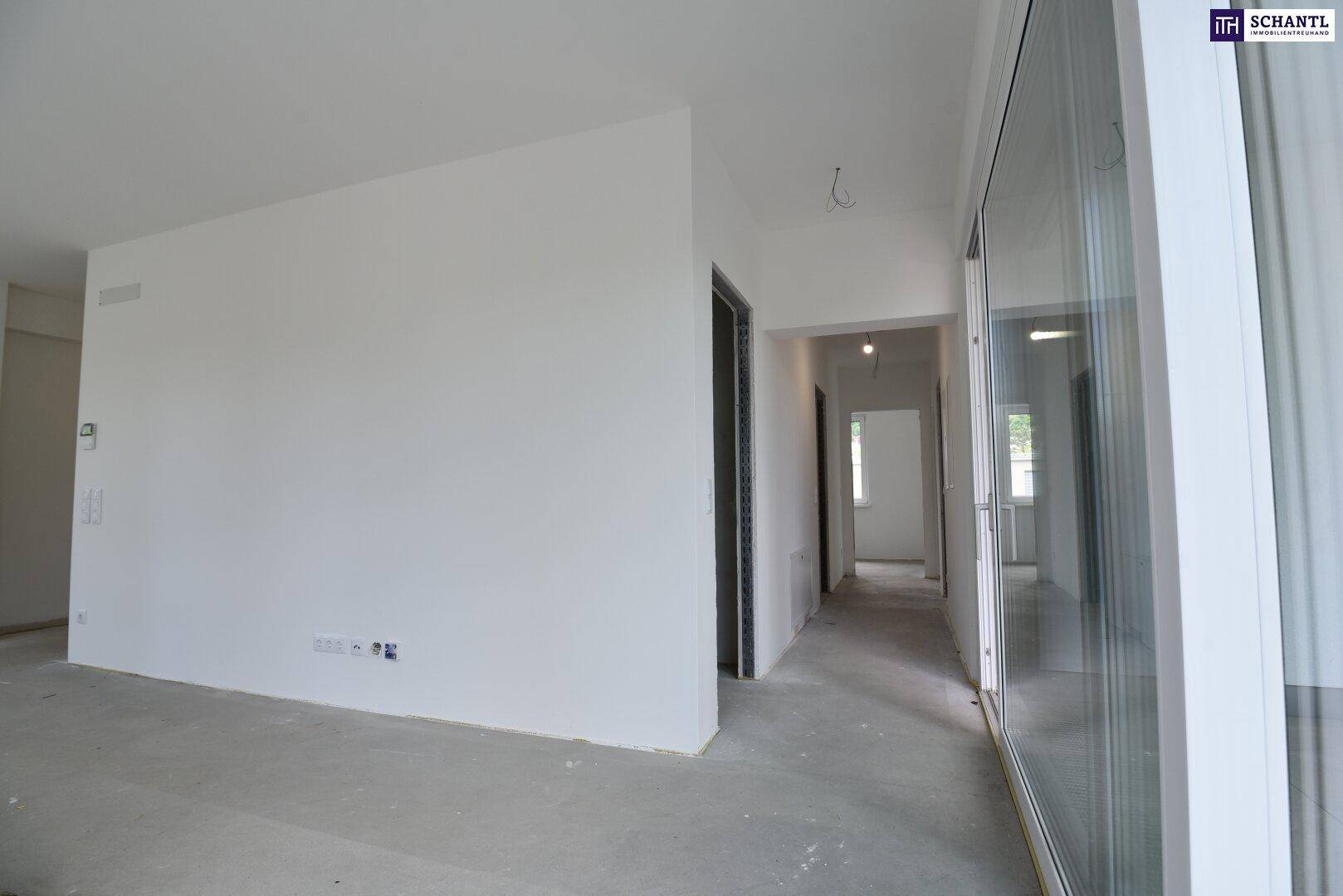 Unfertiger Innenraum mit weißen Wänden, Betonboden und großen Fenstern, bereit für den Ausbau.