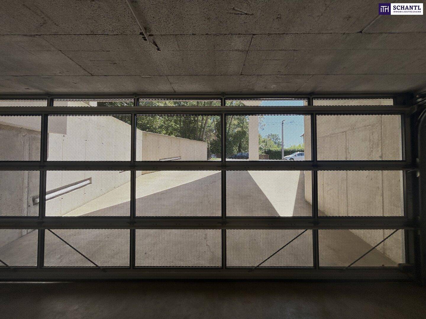 Blick aus der Tiefgarage durch das geschlossene Gittertor auf die Einfahrt und das Tageslicht.