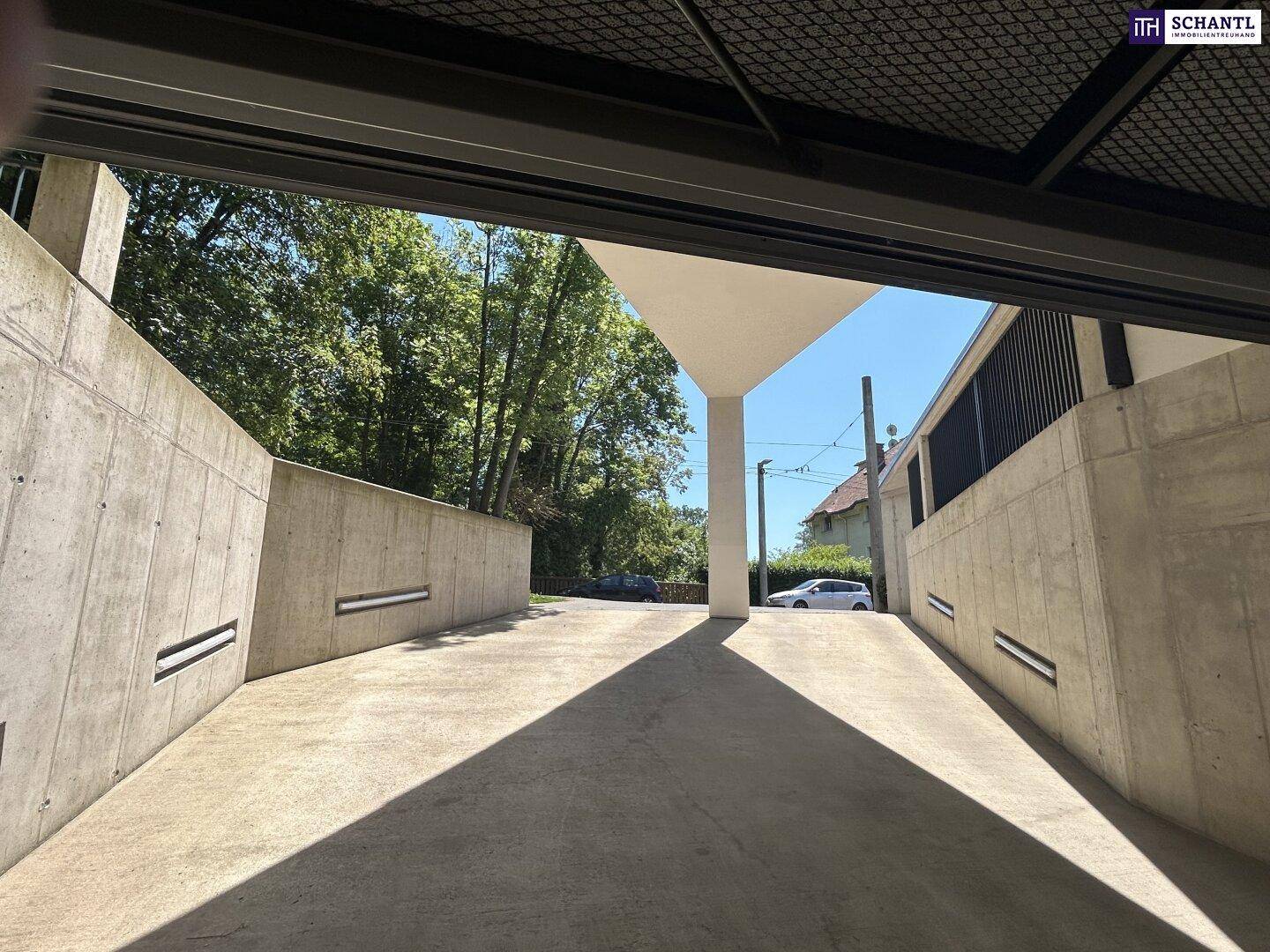 Einfahrt zur Tiefgarage mit Betonwänden und Blick ins Grüne an einem sonnigen Tag.