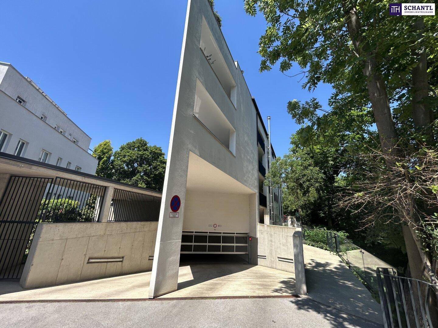 Moderne Architektur des Gebäudes mit der Einfahrt zur Tiefgarage und viel Grün in der Umgebung.