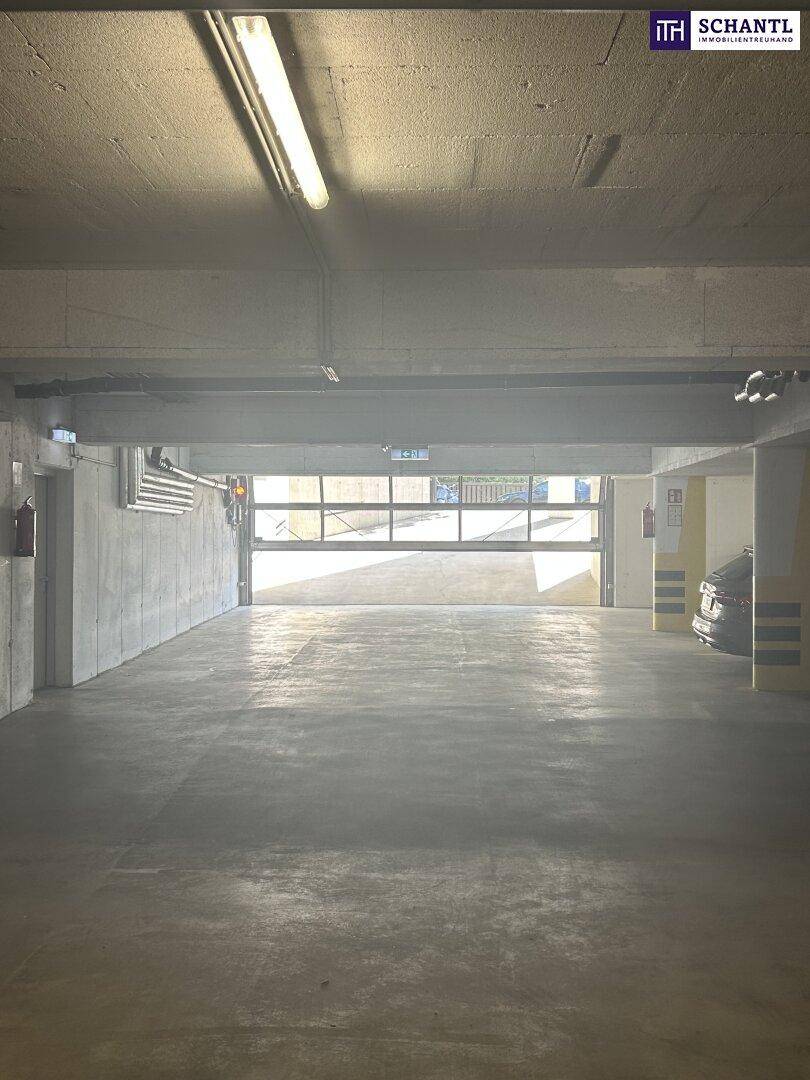 Innenansicht einer Tiefgarage mit Betonwänden, Deckenbeleuchtung und Blick auf das Garagentor.