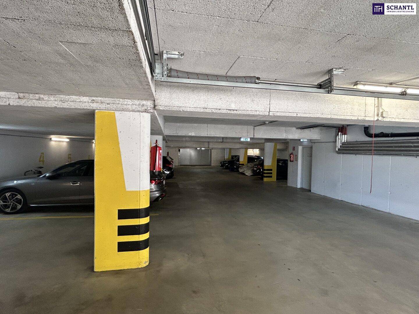 Weitläufige Tiefgarage mit mehreren Parkplätzen, einem Sicherheitspfeiler und Brandschutzausrüstung.