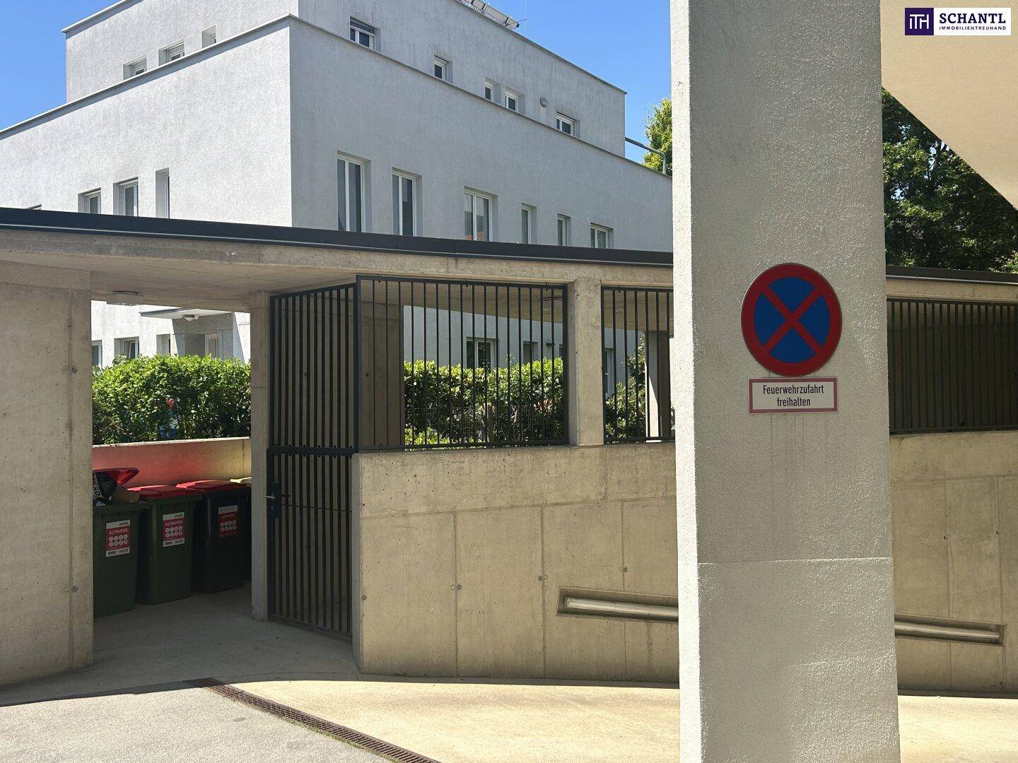 Außenbereich des Gebäudes mit Betonwänden, Mülltonnen und einem Blick auf die Wohnanlage.
