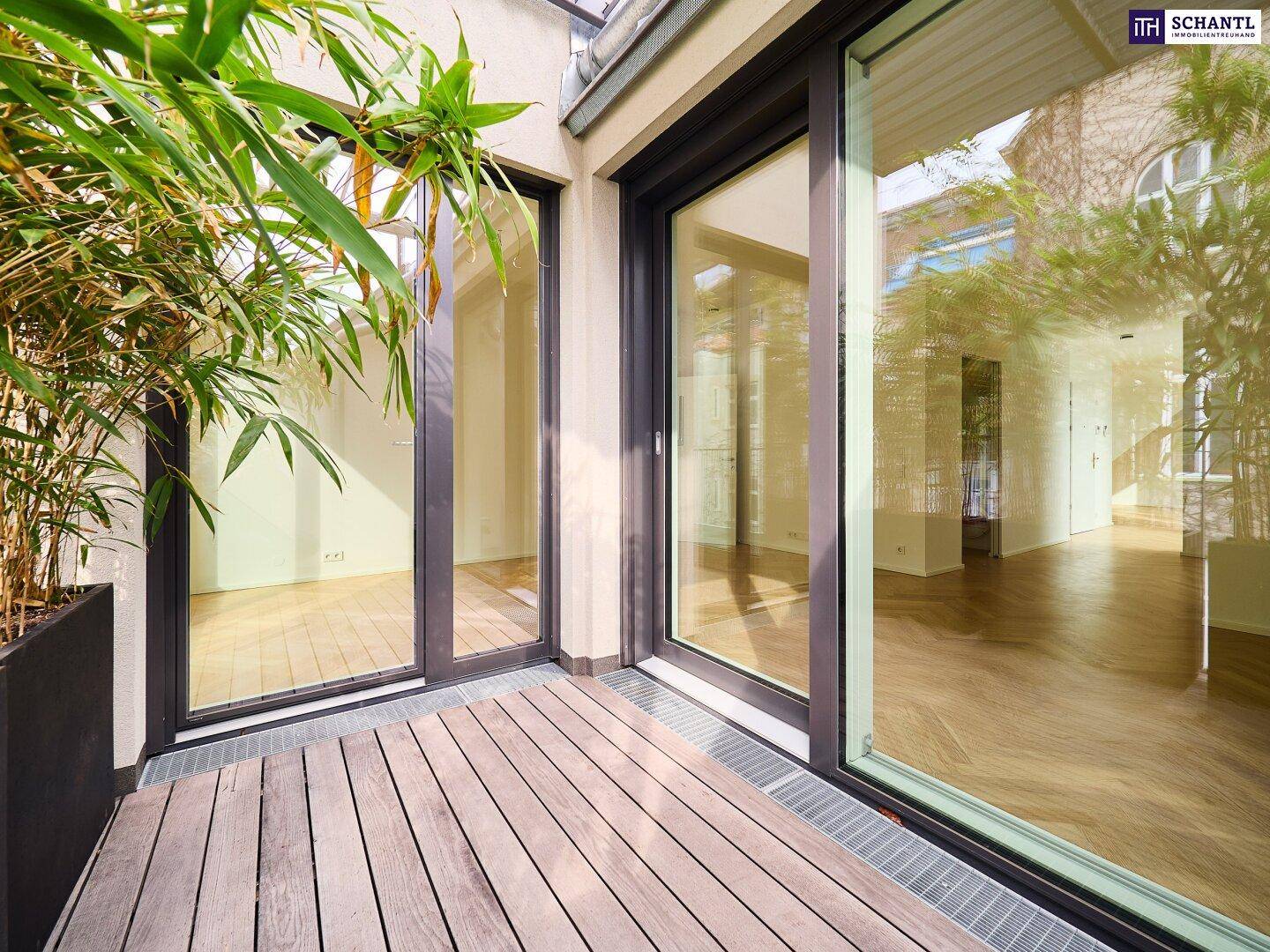 Moderne Terrasse mit Holzboden und großen Glasfronten, die den Innenraum widerspiegeln.